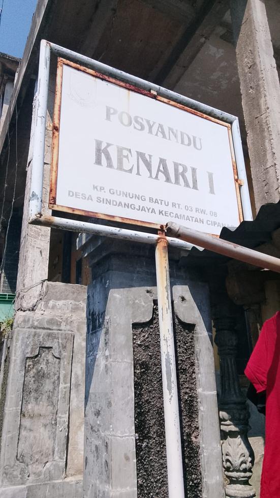 Papan nama Posyandu Kenari I di Kp Gunung Batu, latar penuh pembangunan